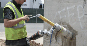 Construction workers operate a core drilling machine on the road, surrounded by safety cones and wearing high-visibility clothing. Equipped with reliable tools like those from US Saws, they ensure precision and safety in every cut.